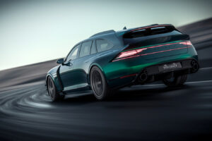 날렵한 녹색 스포츠 왜건 차량이 곡선 도로를 질주하며 뒤에서 바라본 모습입니다. 이 차량은 대담한 라인과 LED 후미등, 뒷면에는 &quot;GENESIS&quot;라는 글자가, 번호판에는 &quot;WINGBACK&quot;이라는 글자가 새겨져 있습니다.