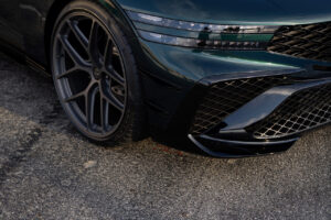 아스팔트 표면에 주차된 대형 알로이 휠, 현대적인 LED 헤드라이트, 세련된 광택 마감을 갖춘 어둡고 날렵한 스포츠카의 왼쪽 전면을 클로즈업합니다.