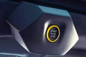 자동차 천장에 노란색 테두리가 있는 기하학적 육각형 모양의 엔진 시동/정지 버튼을 클로즈업하고 중앙에 START ENGINE STOP이라는 문구를 표시합니다.